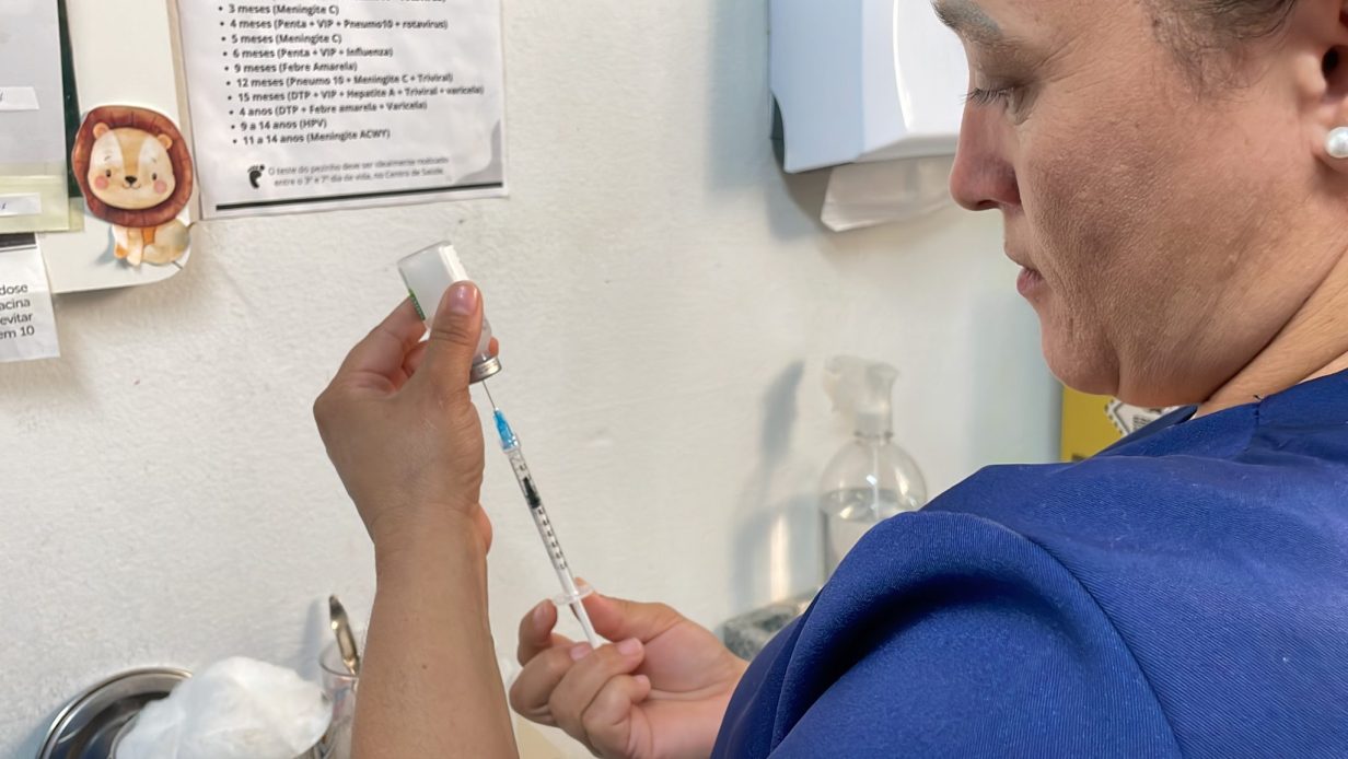 Profissional de saúde prepara seringa com vacina em sala de imunização.